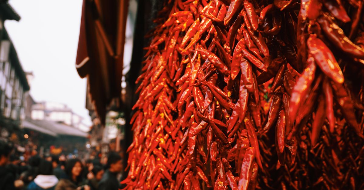 Close-up of red chili peppers in a vibrant street market with bustling crowd.